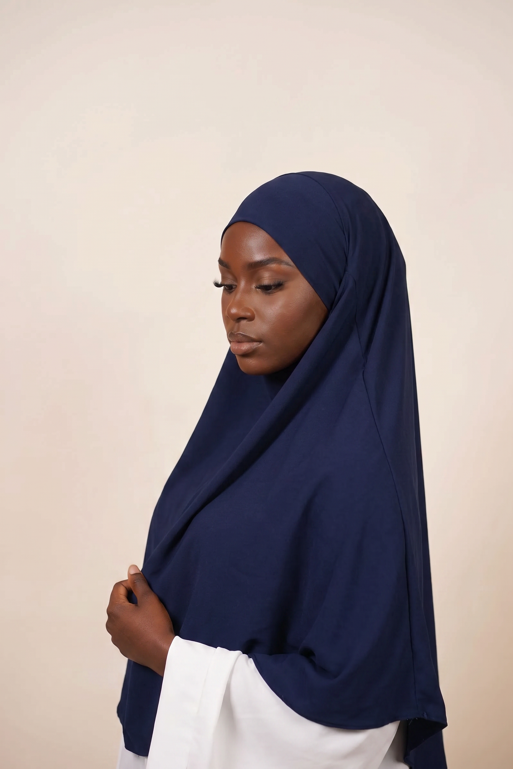 Woman wearing a navy blue hijab against a beige background